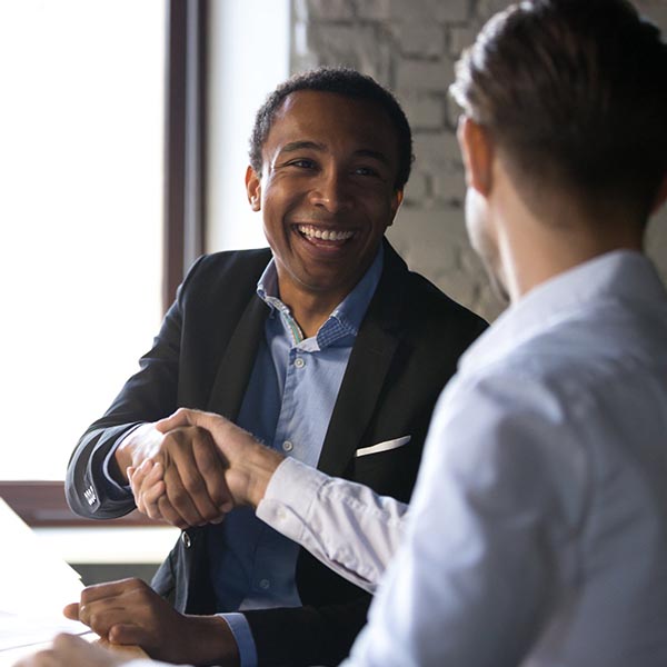 Two people seated at a table shaking hands and smiling.